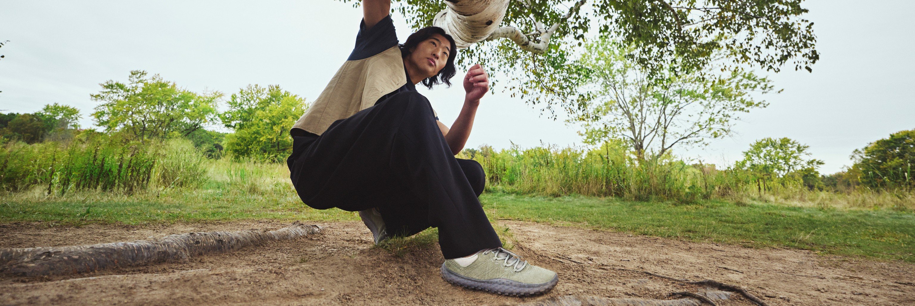 Person crouching under a birch tree wearing Merrell barefoot shoes